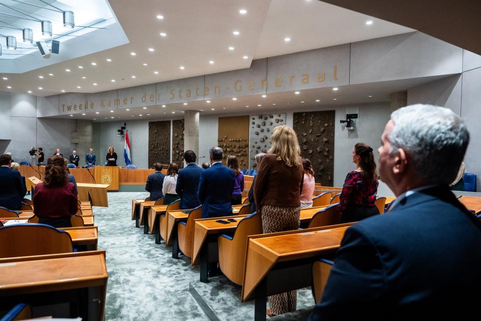 Beeld van achter uit de plenaire zaal, de Kamerleden op de rug gezien. Zij staan tijdens de minuut stilte. Het dichtstbij staat de Israëlische ambassadeur.erdenking,