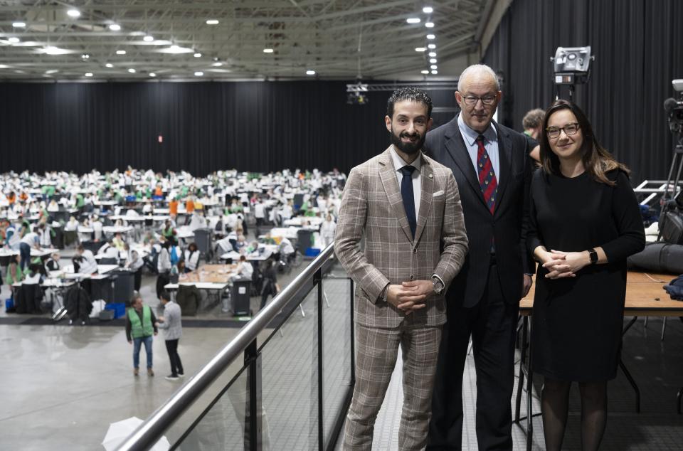 Centrale stemmentelling de Ahoy. Op de voorgrond Kamerleden Ulysse Ellian en Hülya Kat, tussen beiden staat burgemeester Ahmed Aboutaleb. Op de achtergronde staan veel tafels met papieren en stemmentellers.