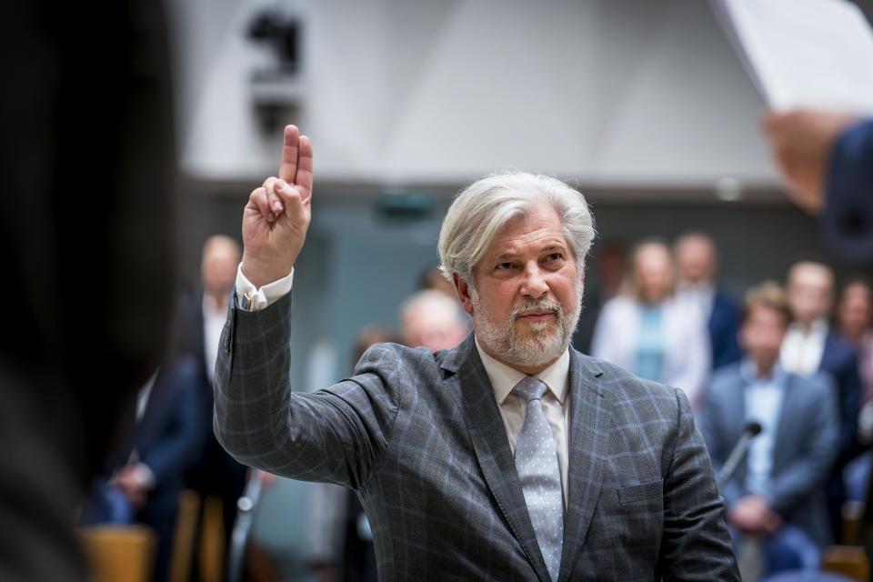 Griffier Peter Oskam houdt twee vingers omhoog tijdens zijn beëdiging in de plenaire zaal. Op de achtergrond staan Kamerleden.