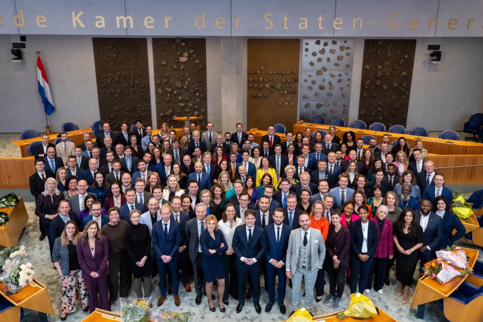 Groepsfoto van alle Kamerleden staand in de plenaire zaal. 