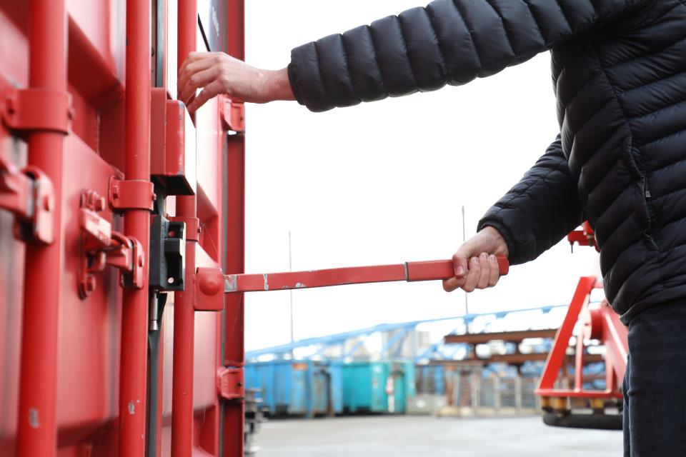 Container die buiten staat en geopend wordt door een persoon met een zwarte jas.