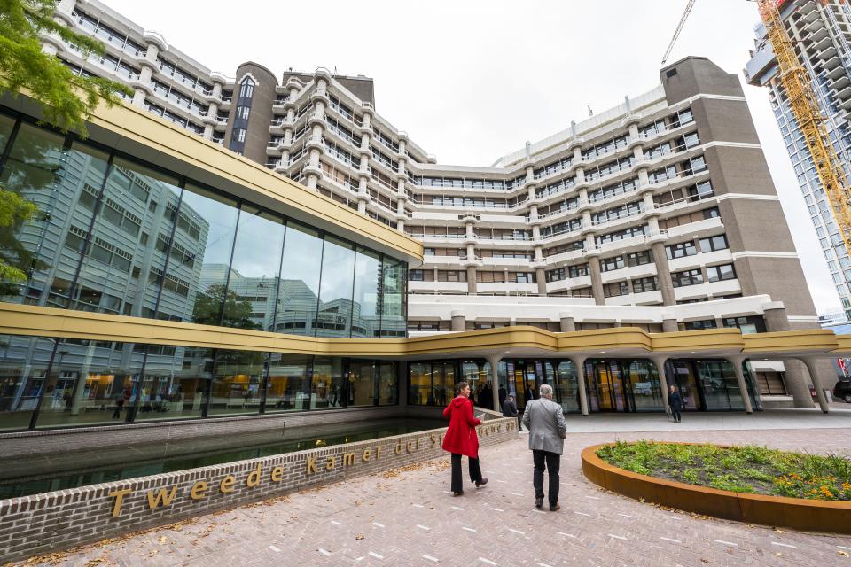 Twee mensen lopen naar het gebouw van de Tweede Kamer toe.