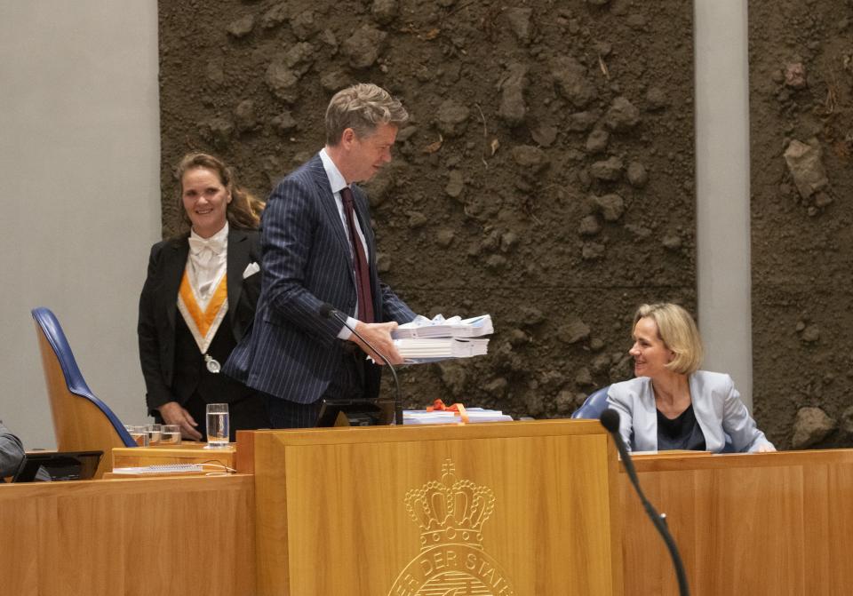 Kamervoorzitter staat in de plenaire zaal en heeft papieren in zijn hand. Achter hem de bode die de stukken aan hem heeft overhandigd. 