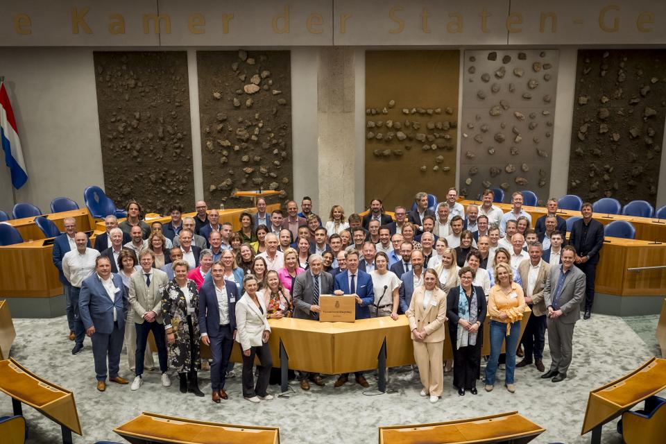 Kamervoorzitter Martin Bosma en Griffier Peter Oskam met de deelnemers aan de V-100 staan in de plenaire zaal van de Tweede Kamer.