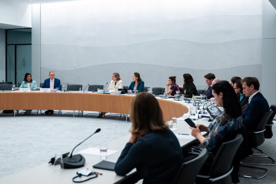 De kandidaat-bewindslieden links aan een gebogen tafel, rechts op de voorgrond de commissieleden. 