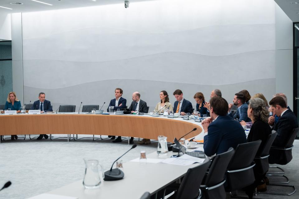 Aan een halfronde tafel zitten links de kandidaat-bewindspersonen voor Buitenlandse Zaken en rechts de commissieleden. 