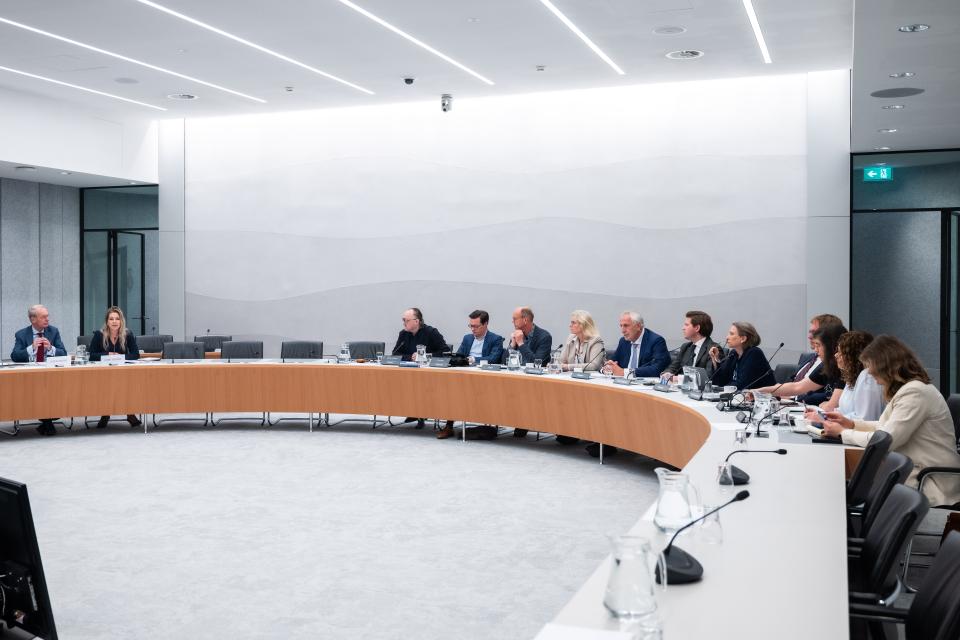 De kandidaat-bewindslieden links aan een gebogen tafel, rechts op de voorgrond de commissieleden. 