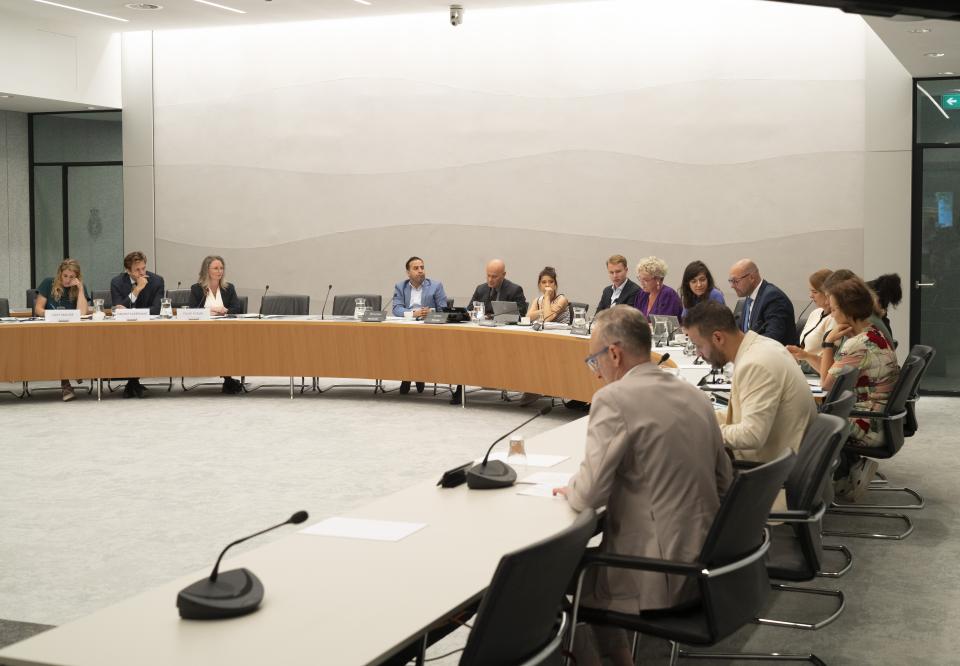 De kandidaat-bewindslieden links aan een gebogen tafel, rechts op de voorgrond de commissieleden. 