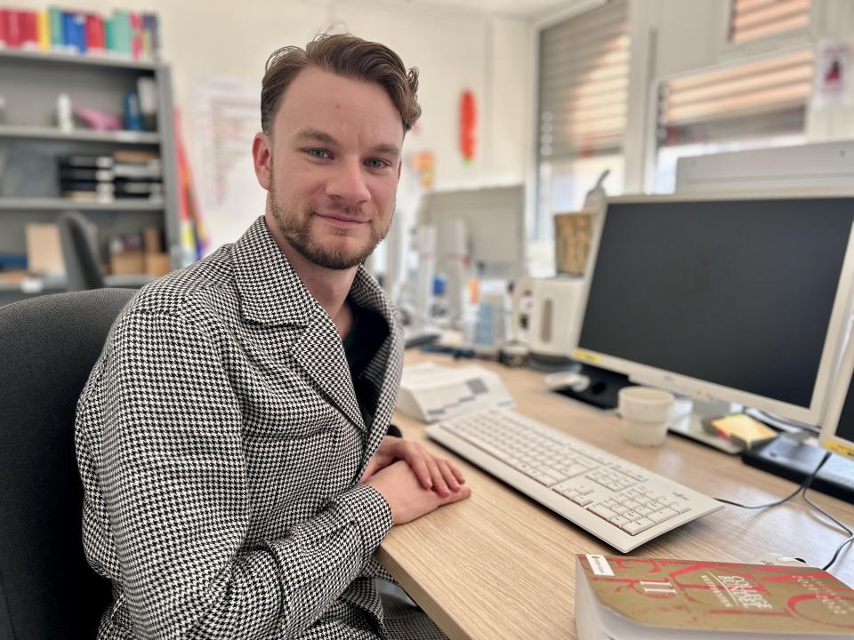 Roelof Bruls zich schuin naar de fotograaf gekeerd achter zijn bureau met computer. 