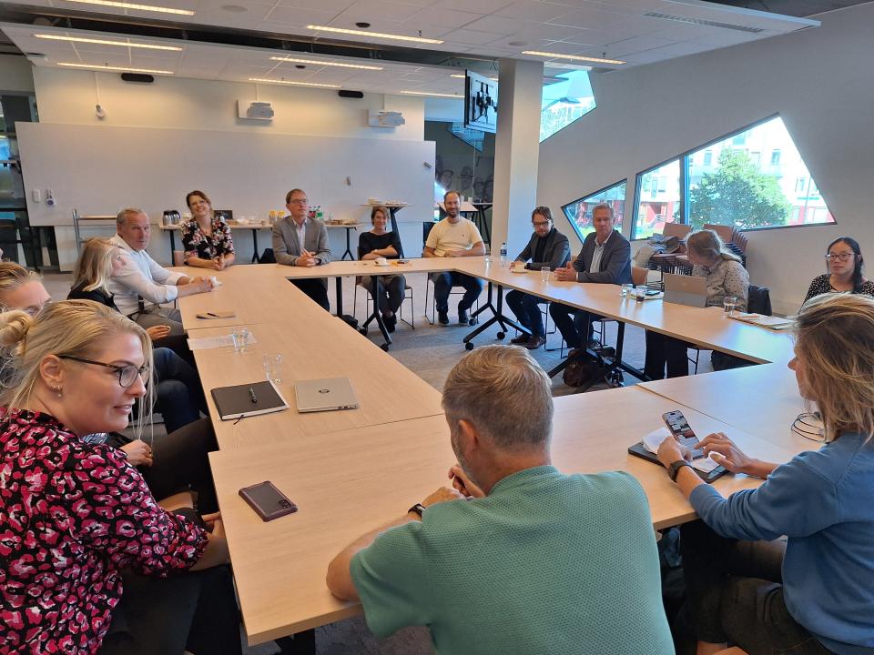 Commissieleden zitten aan een grote tafel en zijn in gesprek met studenten en docenten.