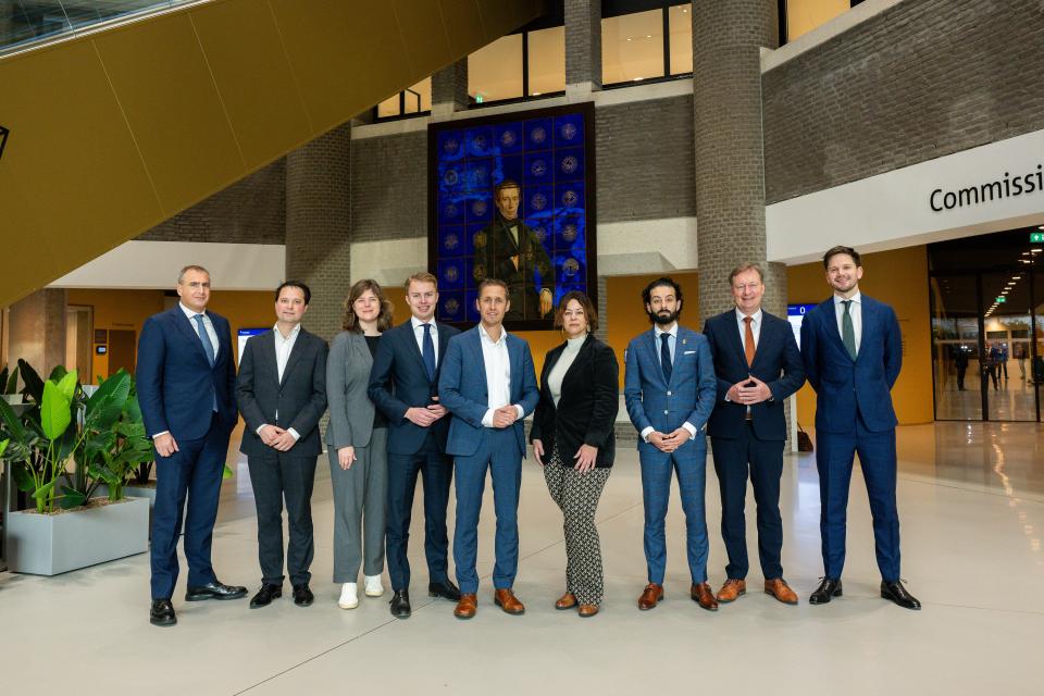 De leden van de commissie poseren in de Statenpassage in een rij naast elkaar voor het kunstwerk over de Grondwet. 