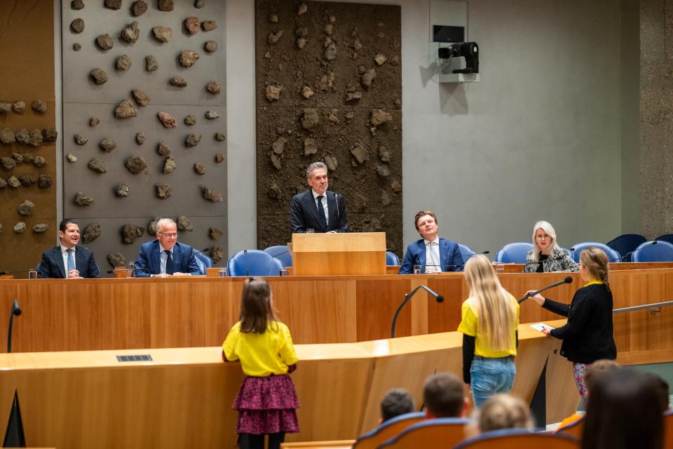 Kinderen staan achter de interuptiemicrofoon en stellen vragen aan minister-president Schoof