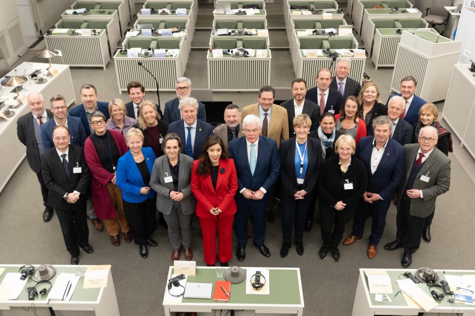 Groepsfoto van bovenaf, de leden staan in het midden van de plenaire zaal van de Eerste Kamer.