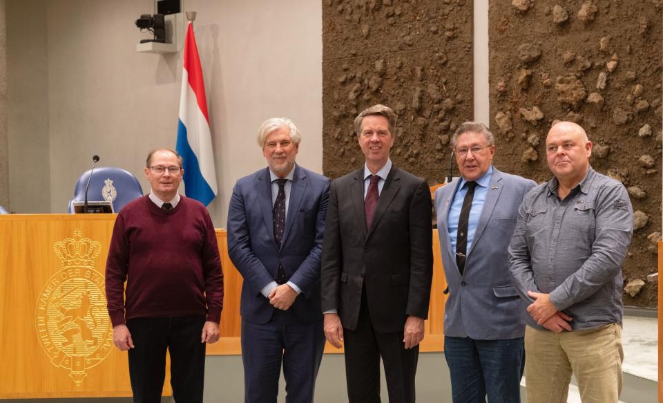 Drie leden van de vereniging poseren met de Voorzitter en de Griffier in de plenaire zaal