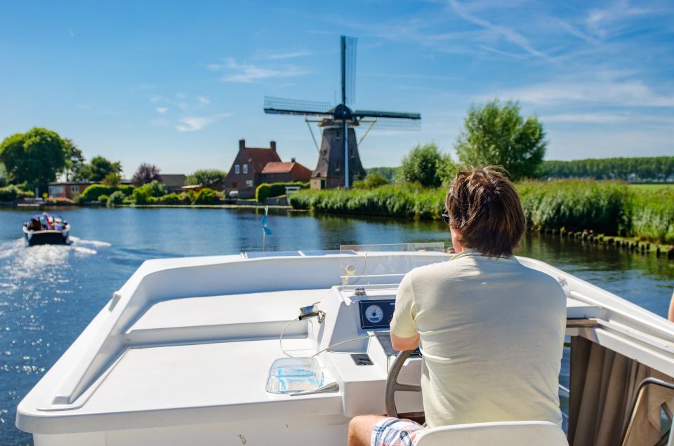 Man vaart in een sloep door de Nederlandse polder langs een molen