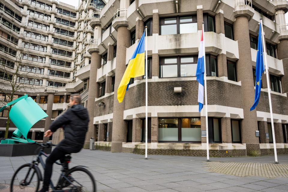 Het tijdelijke gebouw van de Tweede Kamer met links een passerende fietser en in het midden de vlaggen van Oekraïne, Nederland en Europa. 