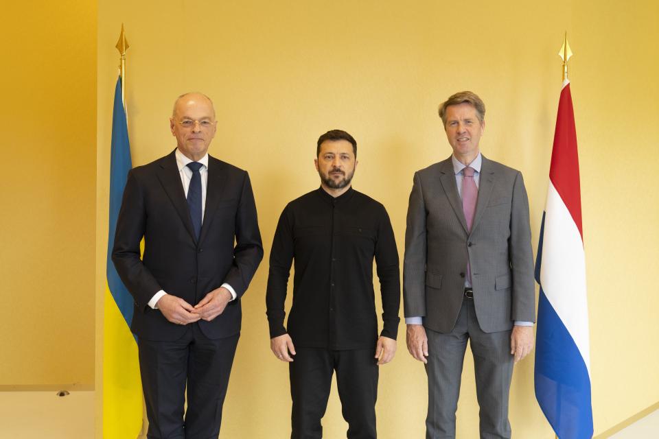 Eerste Kamervoorzitter Jan Anthonie Bruijn, president Volodymyr Zelensky en Tweede Kamervoorzitter Martin Bosma poseren tegen een gele wand tussen twee vlaggen.