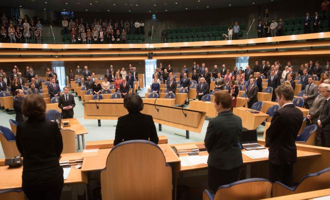 Kamerleden en toeschouwers staan in de vergaderzaal