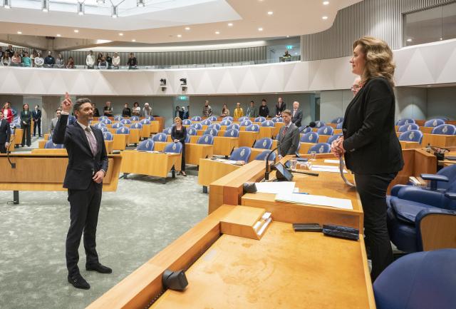 Serge Drost staat in de plenaire zaal met zijn wijs- en middelvinger van zijn rechterhand omhoog om de eed af te leggen ten overstaan van Kamervoorzitter Vera Bergkamp en waarnemend Griffier Geert Jan Hamilton