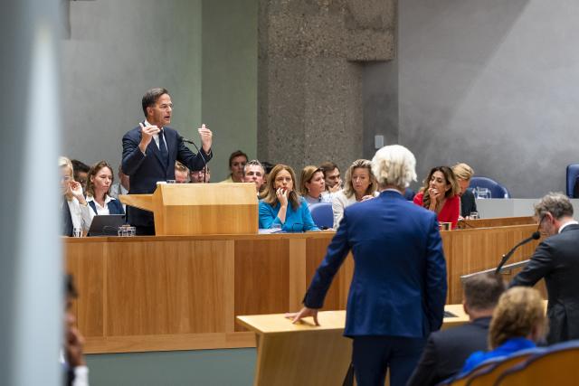 Mark Rutte staat bij het spreekgestoelte van Vak K. Voor hem staan Kamerleden bij de interruptiemicrofoons.