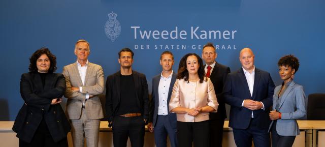 De leden van de parlementaire enquêtecommissie Fraudebeleid en Dienstverlening staan dichtbij elkaar in de Enquêtezaal van de Tweede Kamer.