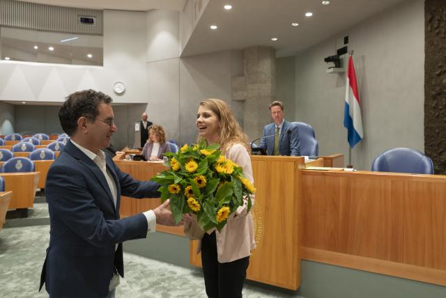 Eva Akerboom staat in de plenaire zaal en ontvangt een bos gele bloemen.