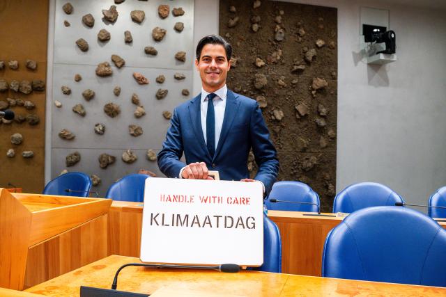 Demissionair minister Rob Jetten in vak K van de plenaire zaal met een koffer waar 'handle with care Klimaatdag' op staat.