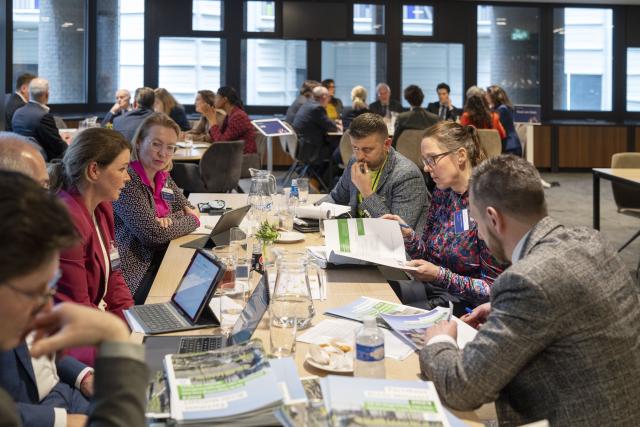 Kamerleden en experts zitten in groepjes aan tafel tijdens de begrotingsbijeenkomst