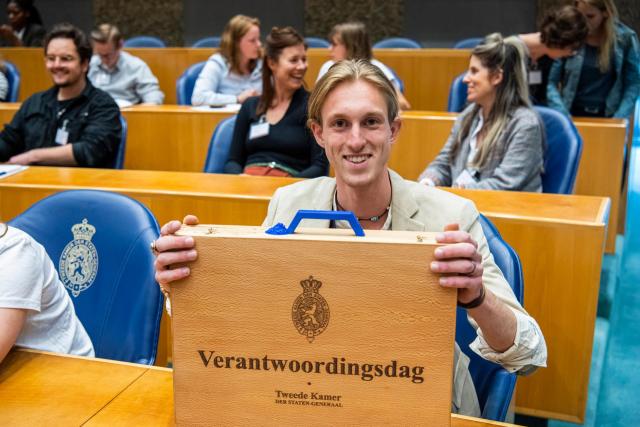 Jongeman laat in Kamerbankje in plenaire zaal een koffertje zien met opschrift Verantwoordingsdag