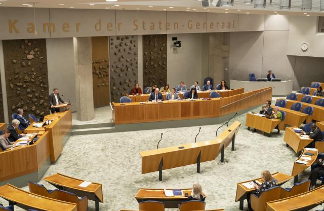 Overzicht van de plenaire zaal. Leden van de parlementaire enquêtecommissie Fraudebeleid en Dienstverlening zitten in vak K en een Kamerlid voert het woord achter het spreekgestoelte. i. 