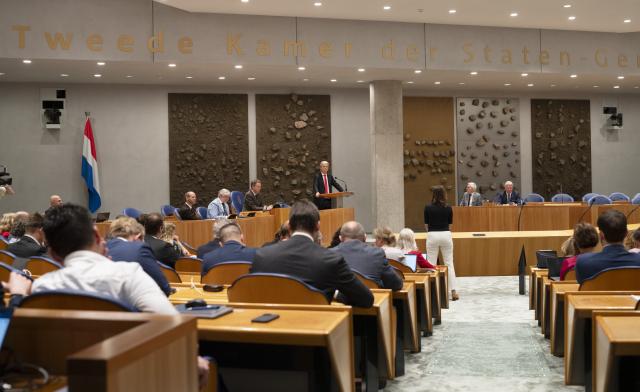 Overzicht in de plenaire zaal. Kamerleden in de bankjes van achteren in beeld, Kamerlid Geert Wilders in het midden aan het spreekgestoelte. 