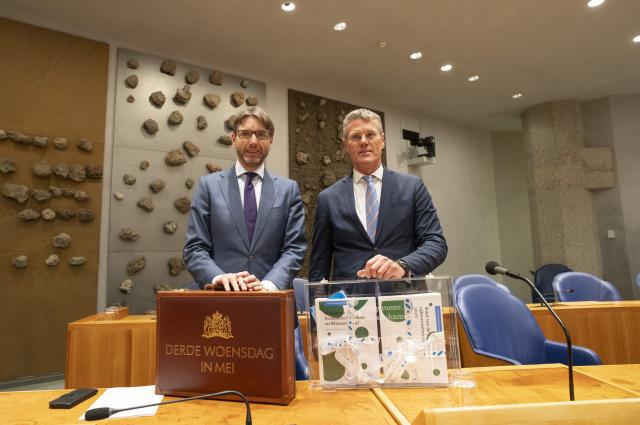 Demissionair minister Steven van Weyenberg van Financiën en de president van de Algemene Rekenkamer, Pieter Duisenberg, staan in vak K in de plenaire zaal. Ze hebben allebei een koffertje voor zich staan.