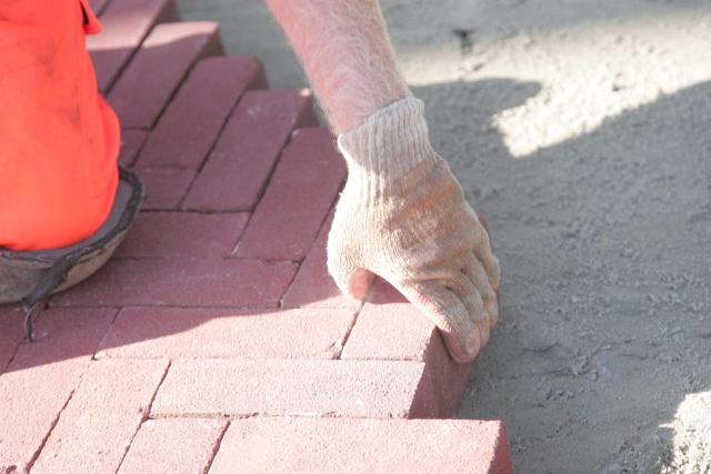 Een hand met handschoen legt klinkers op straat. 