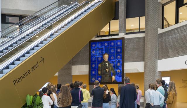 Naast de roltrap in de Statenpassage van de Tweede Kamer kijkt een groep jongeren naar het kunstwerk over de Grondwet dat daar sinds eind 2023 te zien is.