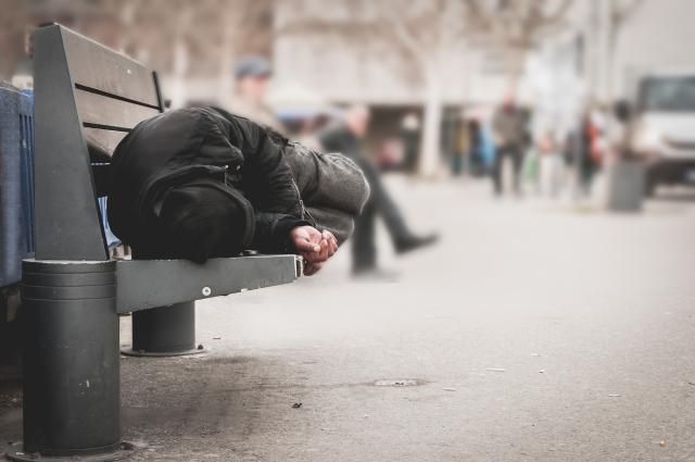 Man ligt op een openbaar bankje op straat te slapen