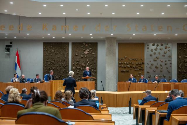 Beeld van de plenaire zaal, van achteren gefotografeerd. Op de rug gezien PVV-fractievoorzitter Geert Wilders bij de interruptiemicrofoon en GroenLinks-PvdA-fractievoorzitter Frans Timmermans achter het spreekgestoelte. 