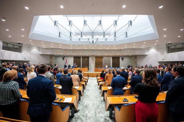 Kamerleden staan in de plenaire zaal tijdens de herdenking van Hans Wiegel.